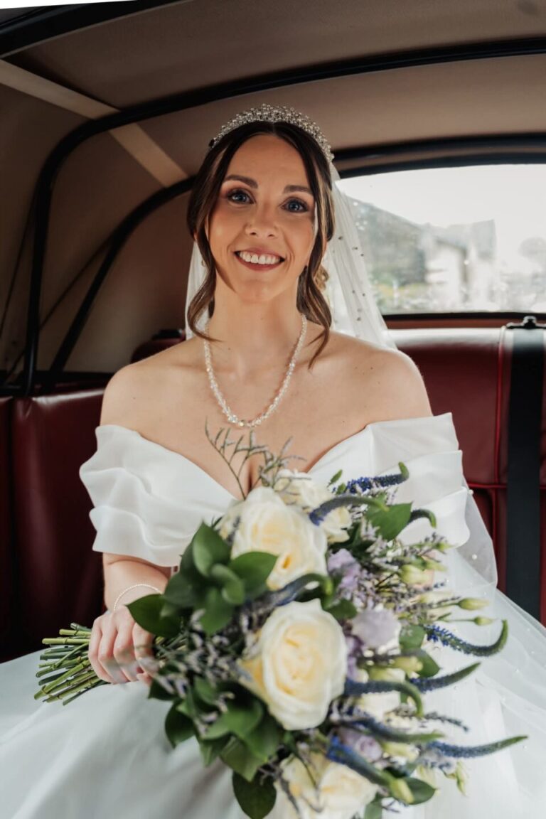 Bride arriving in vintage wedding car at Stirk House Hotel Gisburn holding white rose bouquet