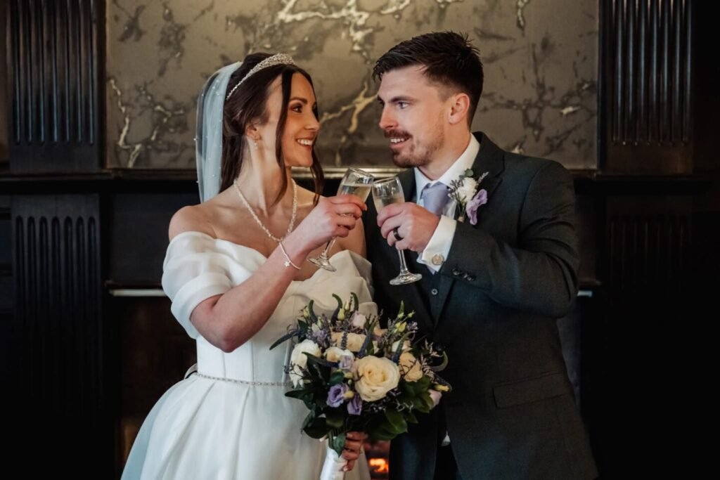 Lucy and Lewis toasting champagne in front of the historic marble fireplace inside Stirk House.