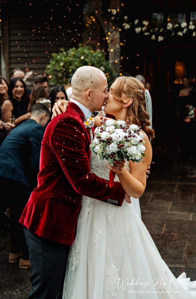 Romantic kiss under a shower of confetti for Katie and Mathew outside the rustic barn at The Oak Tree of Peover