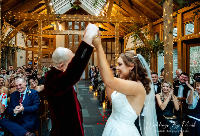 Newlyweds Katie and Mathew raising their hands in celebration inside the ceremony room at The Oak Tree of Peover