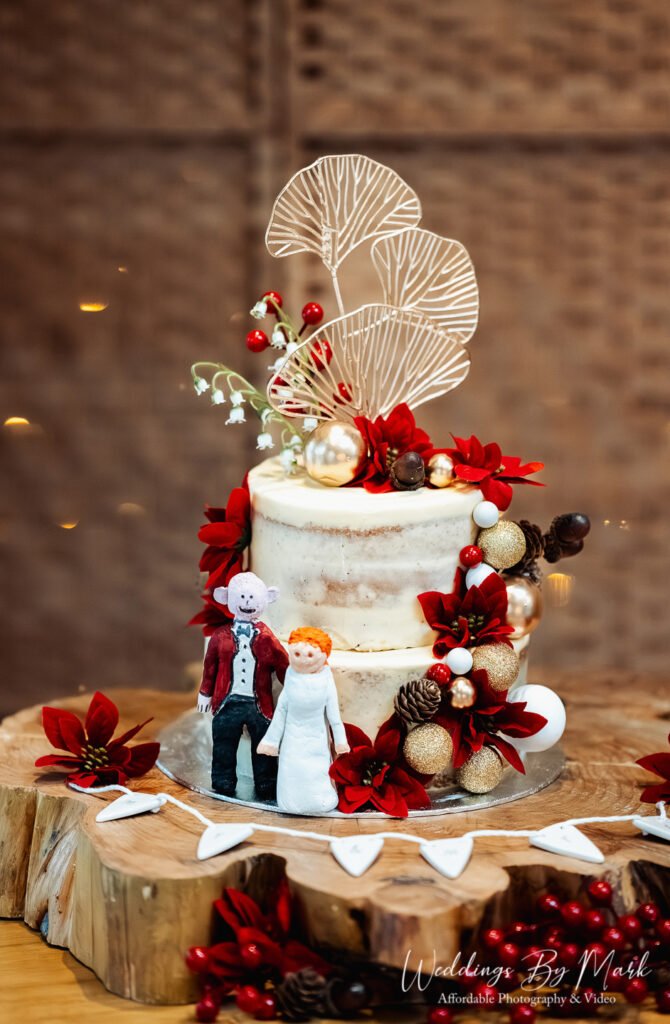 Unique wedding cake featuring custom toppers and festive red floral details at The Oak Tree of Peover