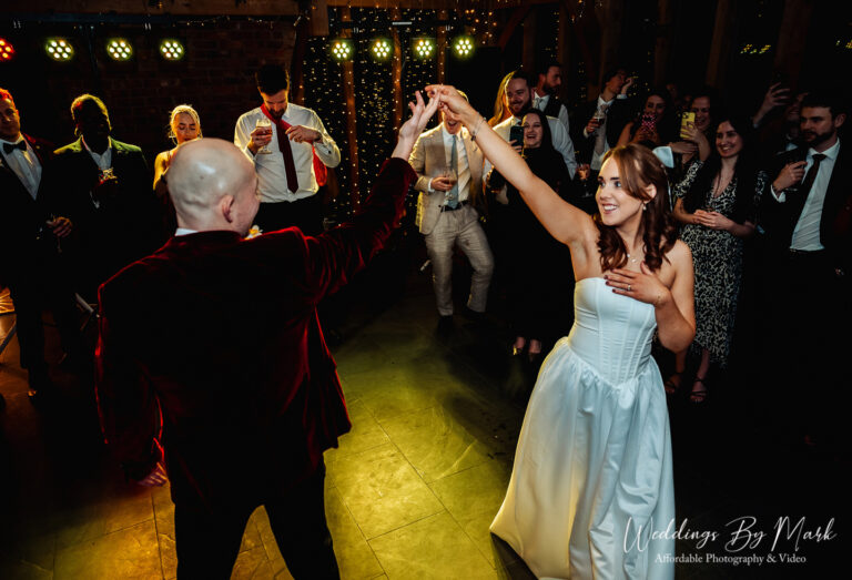 AA vibrant color shot of the first dance. The couple is in the center of the dance floor surrounded by twinkling lights and guests, with the groom dipping or spinning the bride