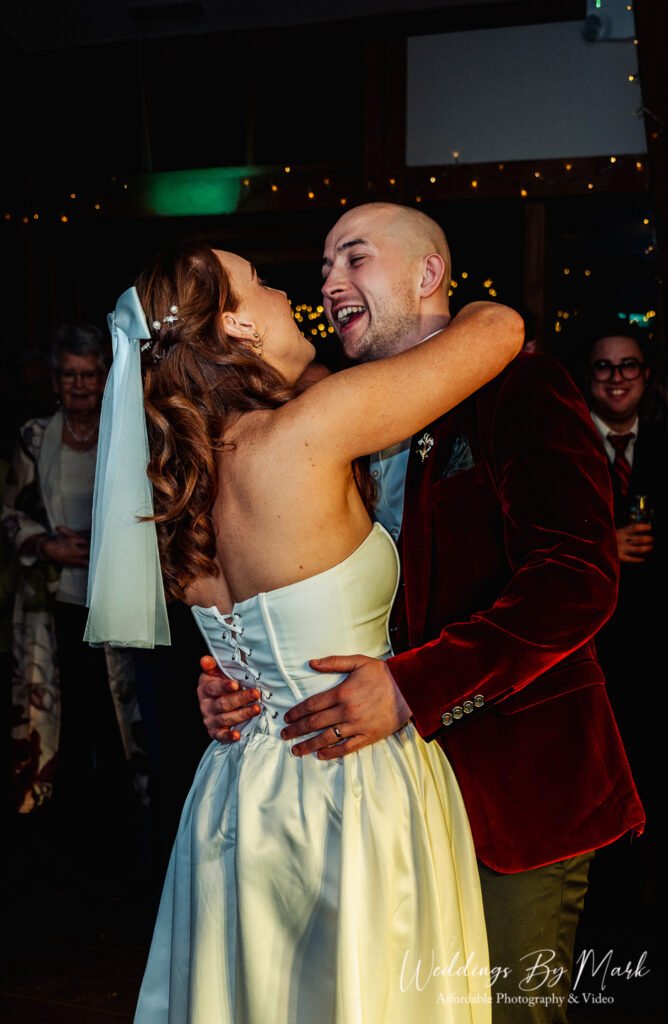 A lovely, intimate close-up of the couple hugging and laughing on the dance floor, capturing a genuine moment of connection amidst the party