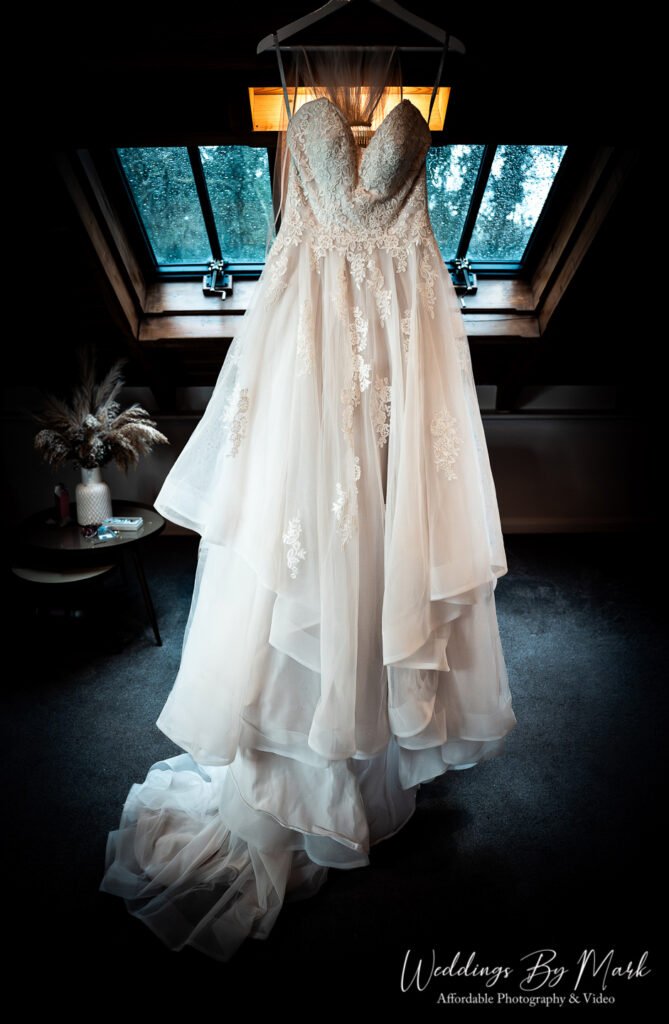 Elegant lace wedding dress hanging in the window light of the bridal suite at The Oak Tree of Peover