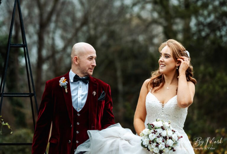 Mathew in a stylish red velvet suit looking lovingly at Katie during their wedding photography session at The Oak Tree of Peover