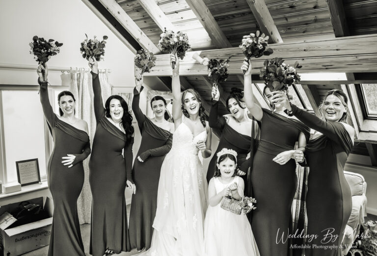 Black and white candid shot of bridesmaids cheering with bouquets, showcasing natural wedding photography at The Oak Tree of Peover