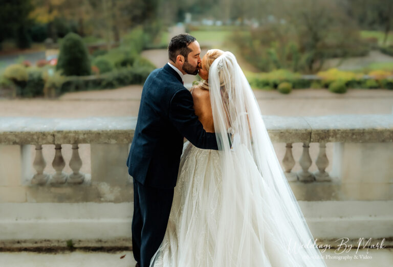 Maria and Jonny sharing a kiss on the balcony at Eaves Hall with panoramic views of the Lancashire countryside.