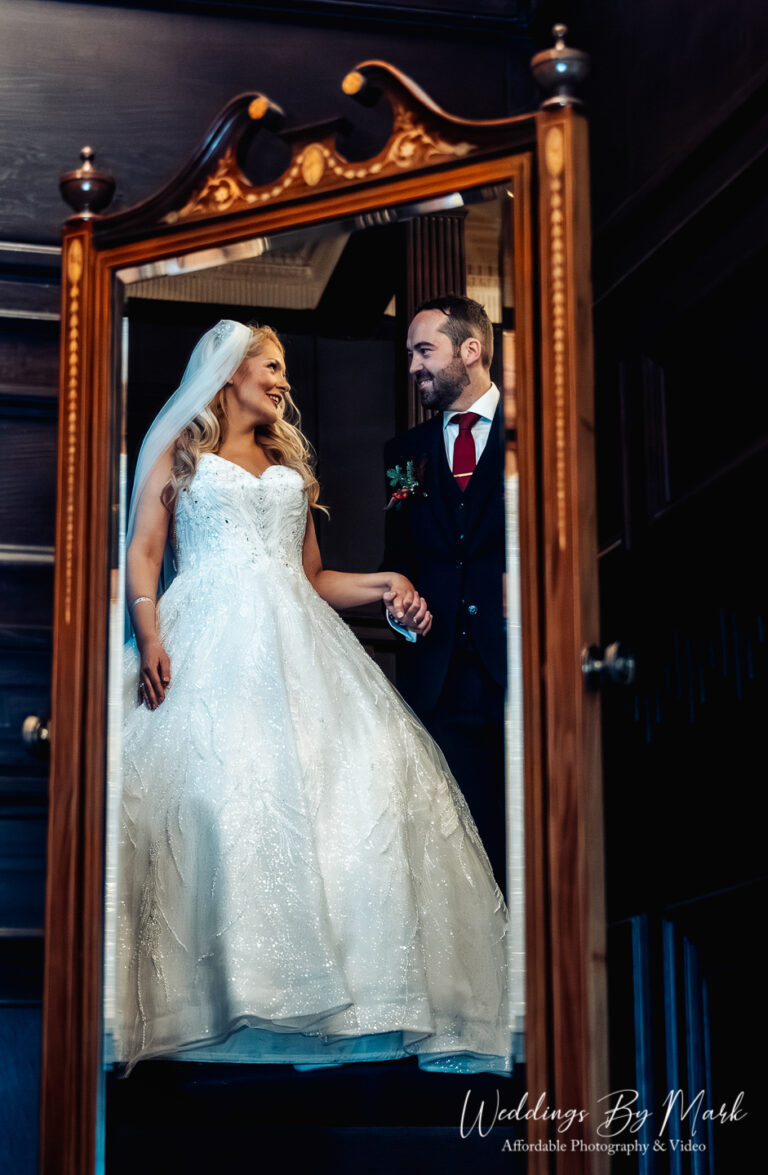Creative reflection portrait of the bride and groom in the large mirror on the grand staircase at Eaves Hall.