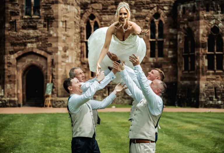 Fun and relaxed wedding photo of the groom and groomsmen lifting the bride into the air on the lawns of Peckforton Castle.