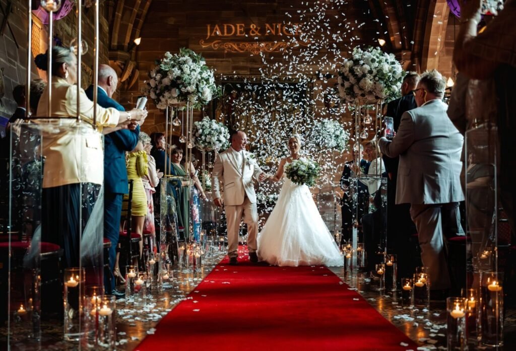 Joyful confetti moment as Jade and Nick walk down the aisle after their wedding ceremony in the Great Hall at Peckforton Castle.