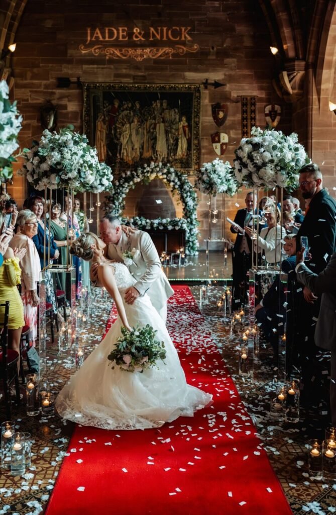 Romantic dip kiss for the bride and groom on the red carpet aisle of the Great Hall at Peckforton Castle, captured by a Cheshire wedding photographer.